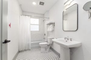 Bacthroom with black and white tile floor, pedistal sink, and bath/shower unit.